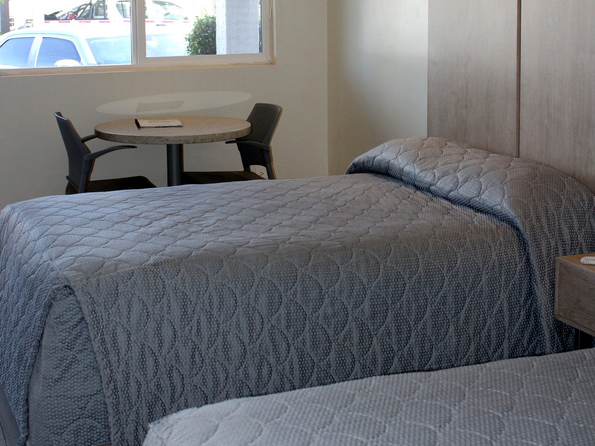 Habitación doble remodelada: cama con cubrecama azul y mesa redonda junto a la ventana