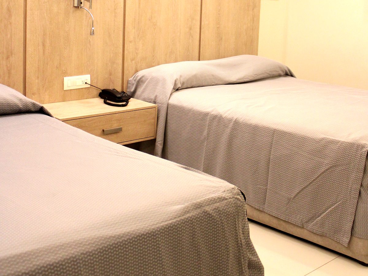 Habitación doble remodelada: dos camas con cabecera de madera clara y buró