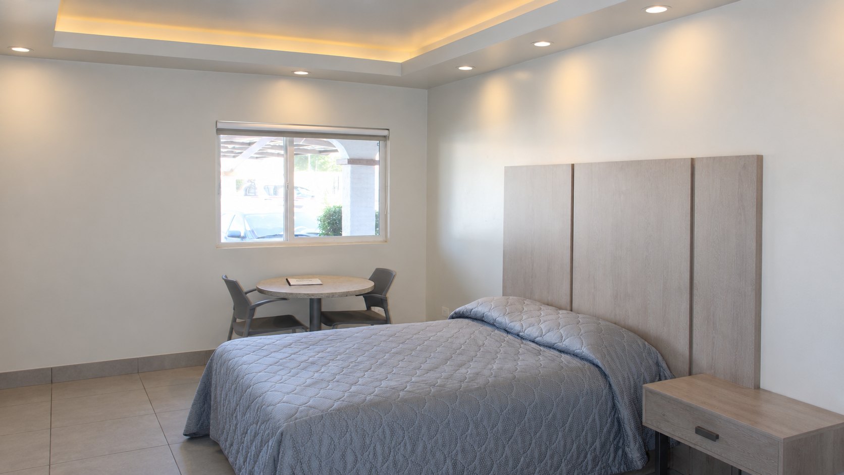 Habitación remodelada de La Siesta: la cama, la mesa junto a la ventana y el plafón con su luz