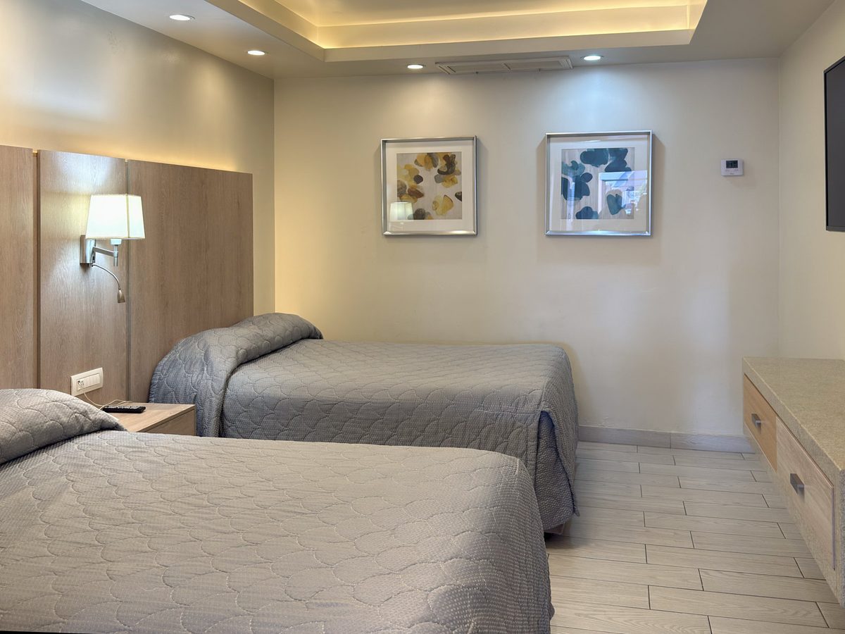 Junior Suite bedroom: two beds with light-wood headboards, prints and indirect lighting