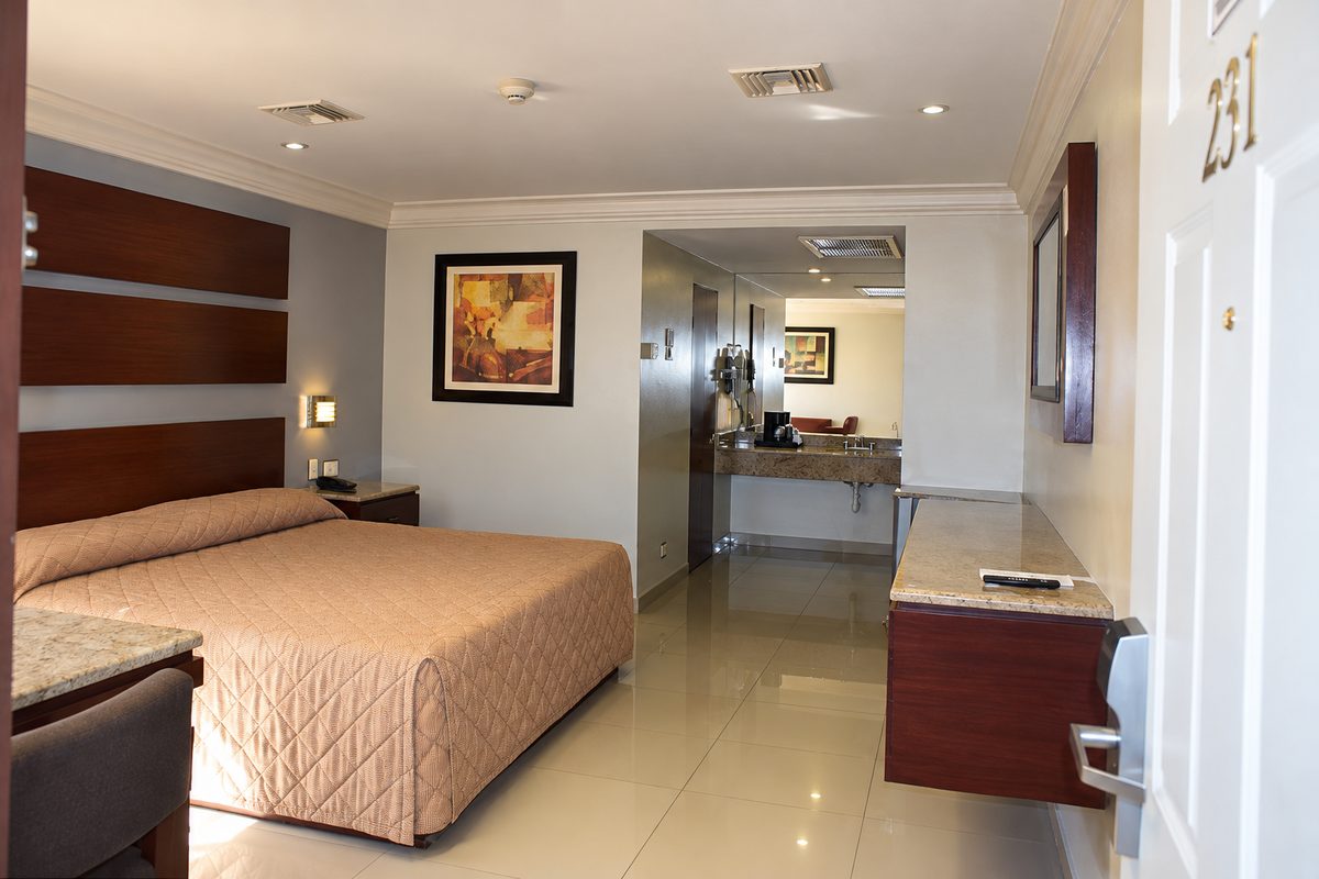Habitación sencilla vista desde la puerta: cama King, escritorio y el pasillo al baño