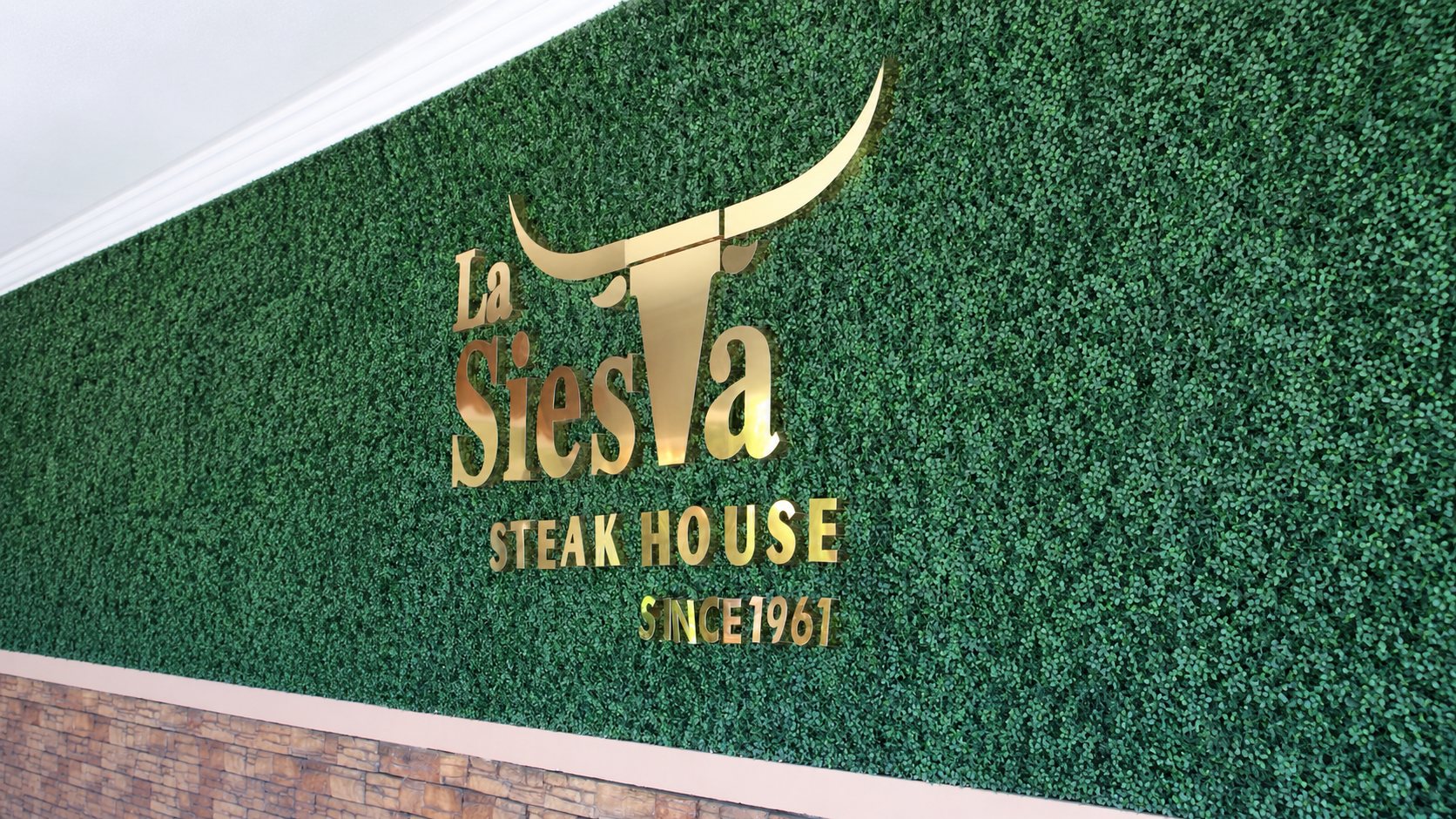 El muro de follaje con el logotipo dorado de La Siesta Steakhouse